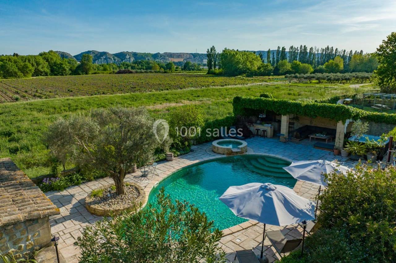 Vue d'une piscine entourée de végétation, avec un jacuzzi, des parasols et un paysage de campagne en arrière-plan.