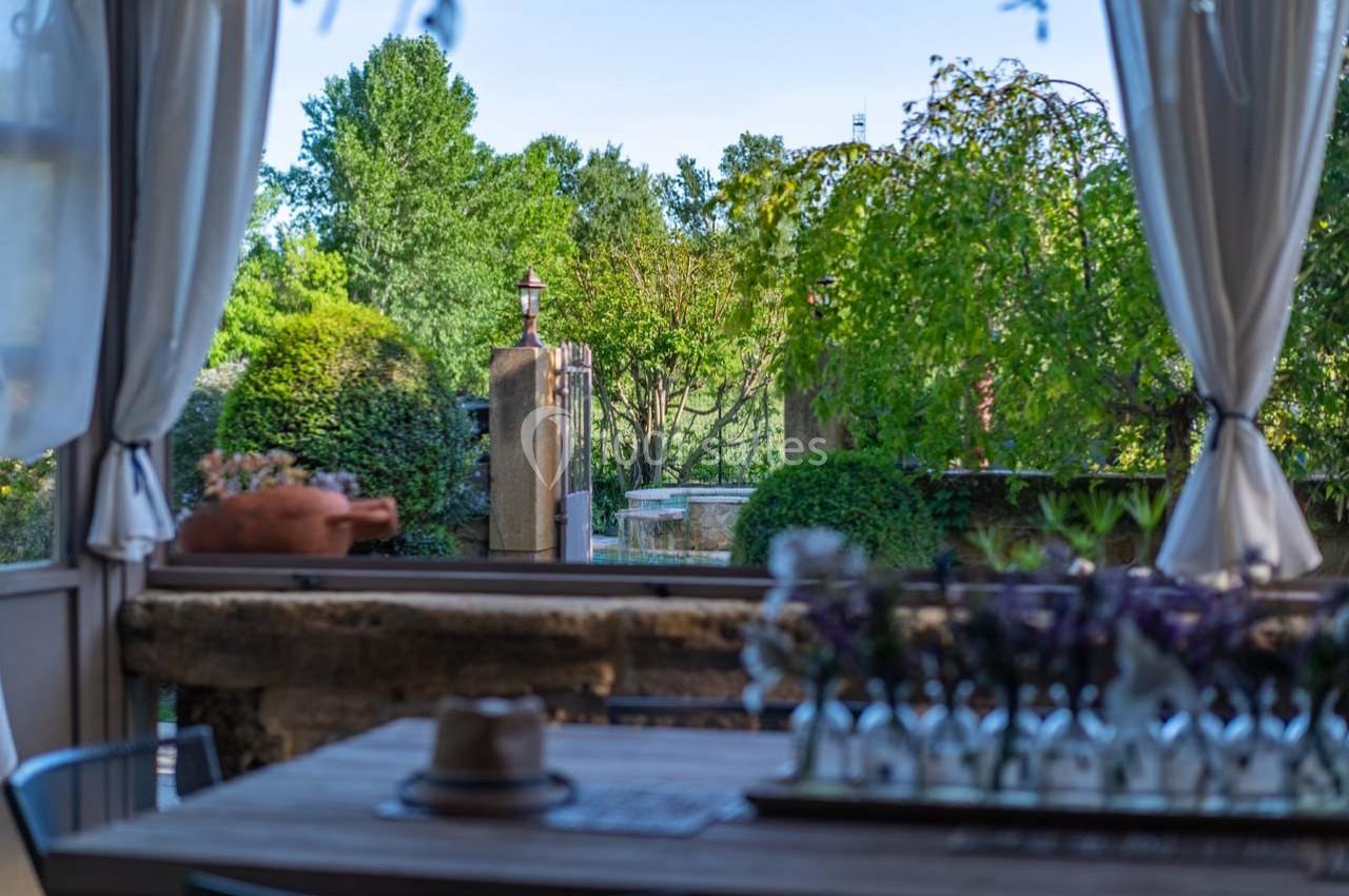 Vue d'une terrasse ombragée avec table en bois, donnant sur un jardin verdoyant et des arbres en arrière-plan.