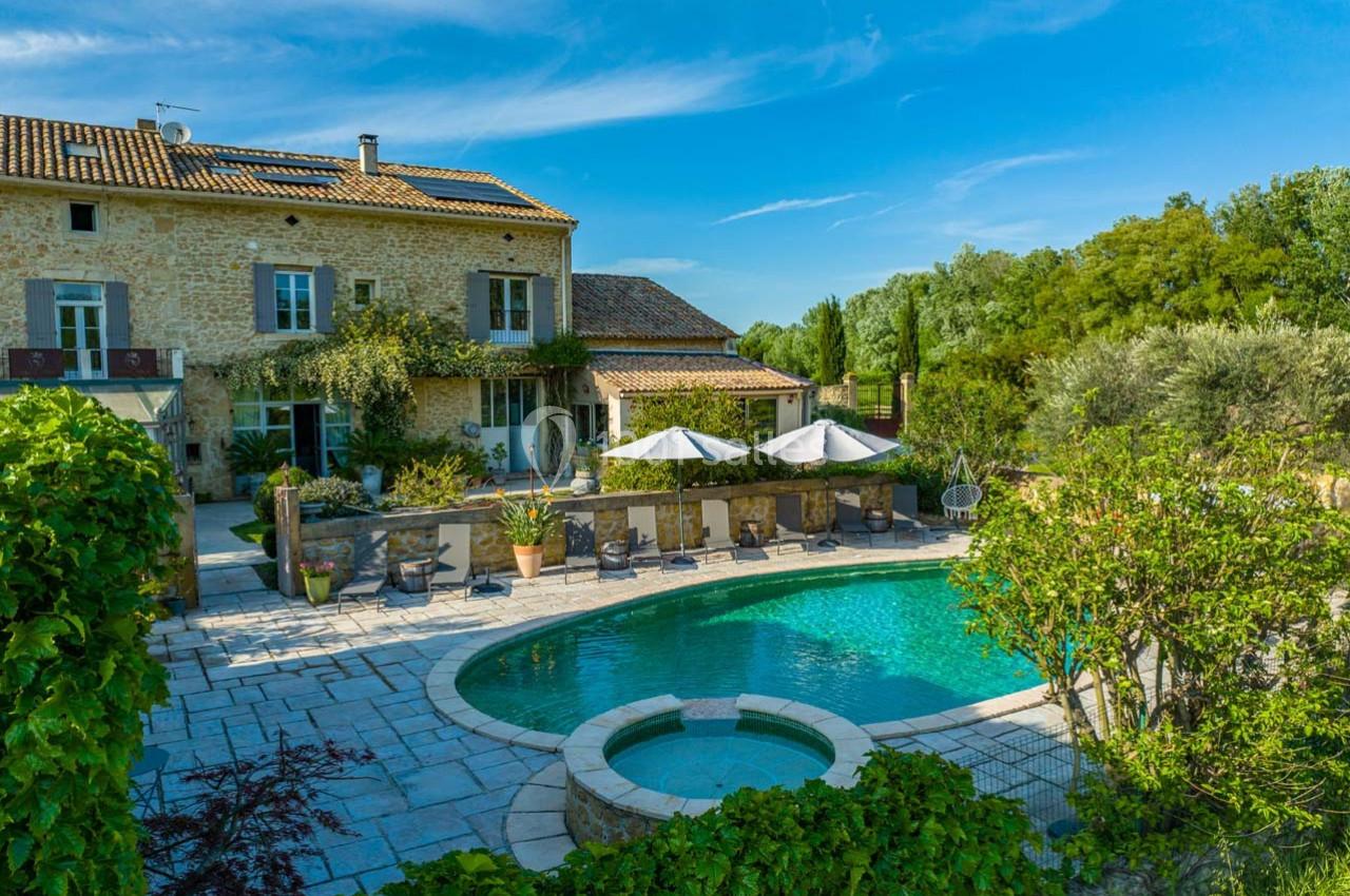 Maison en pierre avec piscine entourée de végétation, terrasse aménagée et ciel dégagé en arrière-plan.