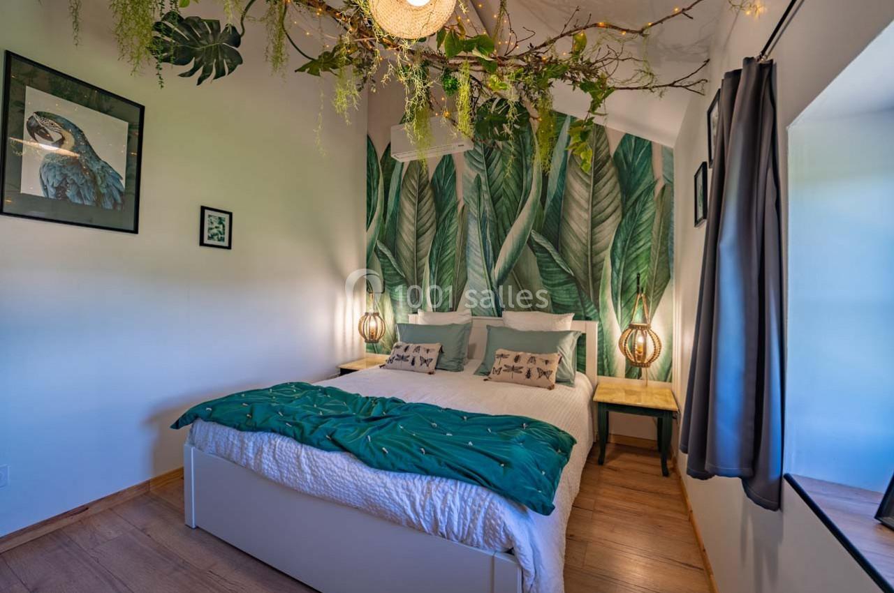 Chambre lumineuse avec lit double, décoration murale tropicale, plantes suspendues et éclairage chaleureux.
