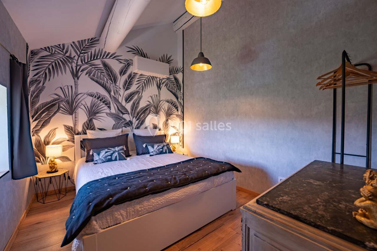 Chambre moderne avec lit double, mur décoré de motifs végétaux, éclairage suspendu et mobilier en bois.