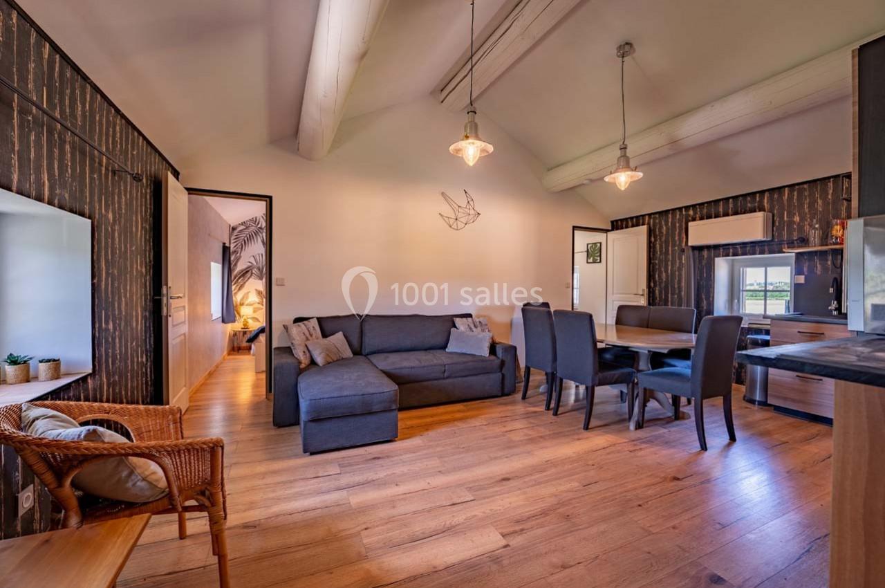 Salon lumineux avec canapé gris, table à manger, cuisine ouverte et décoration en bois dans un intérieur moderne.