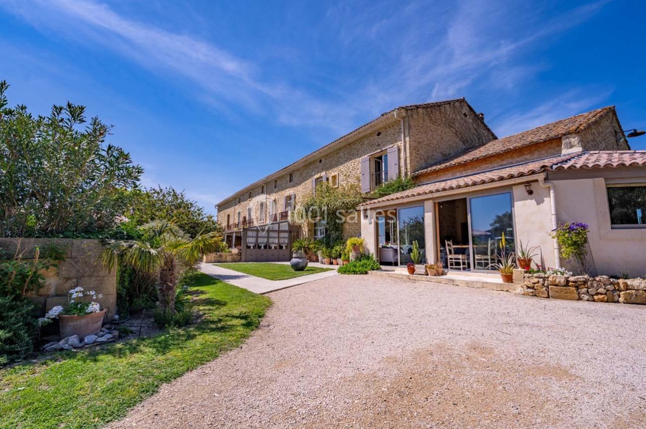 Façade d'une maison en pierre avec jardin, terrasse et ciel dégagé en arrière-plan.