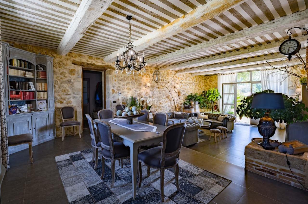 Salle à manger rustique avec murs en pierre, poutres apparentes, table en bois, chaises élégantes et lumière naturelle.
