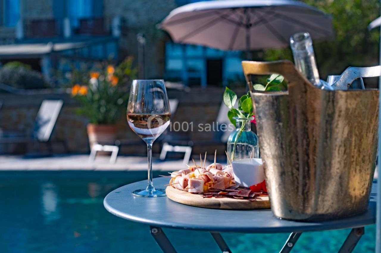 Verre de vin rosé, plateau de charcuterie et seau à glace sur une table près d'une piscine en extérieur.