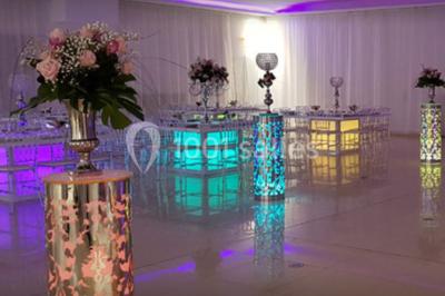 Salle de réception élégante avec tables dressées, chaises décorées et une estrade ornée de rideaux lumineux.