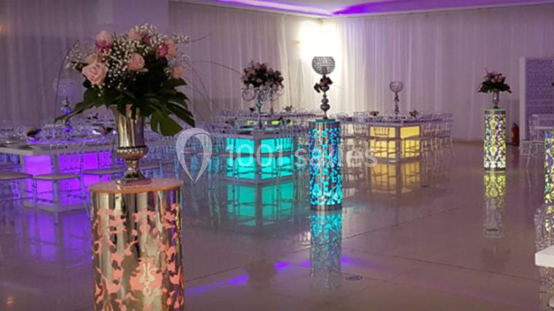 Salle de réception décorée avec des tables illuminées, des colonnes ornées et des arrangements floraux.