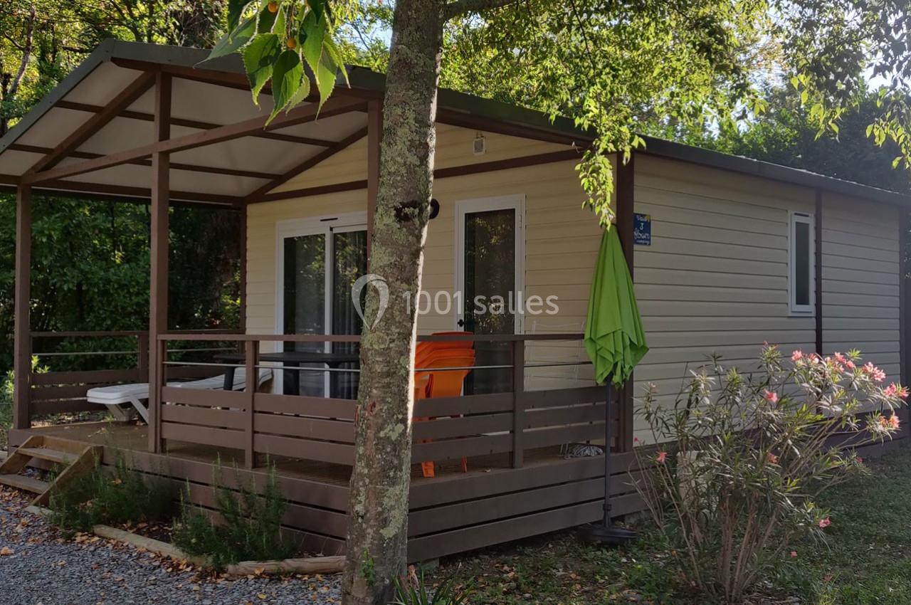 Chalet en bois clair avec terrasse couverte, entouré de végétation et équipé de mobilier extérieur.