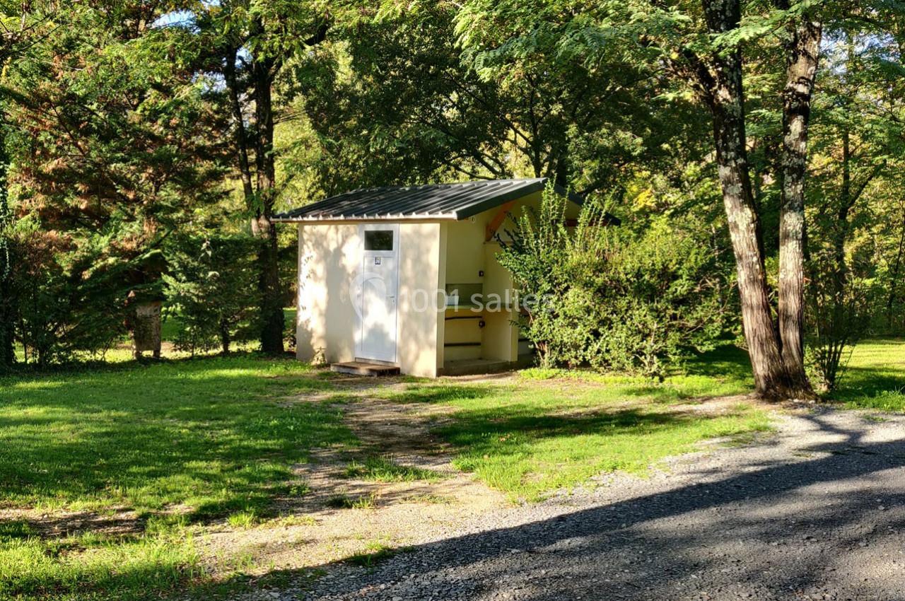 Abri en béton avec toit en pente, entouré d'arbres et de buissons, situé dans un espace verdoyant.