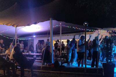 Salle de réception en extérieur décorée pour un événement, avec tables dressées, fleurs et voilages suspendus.