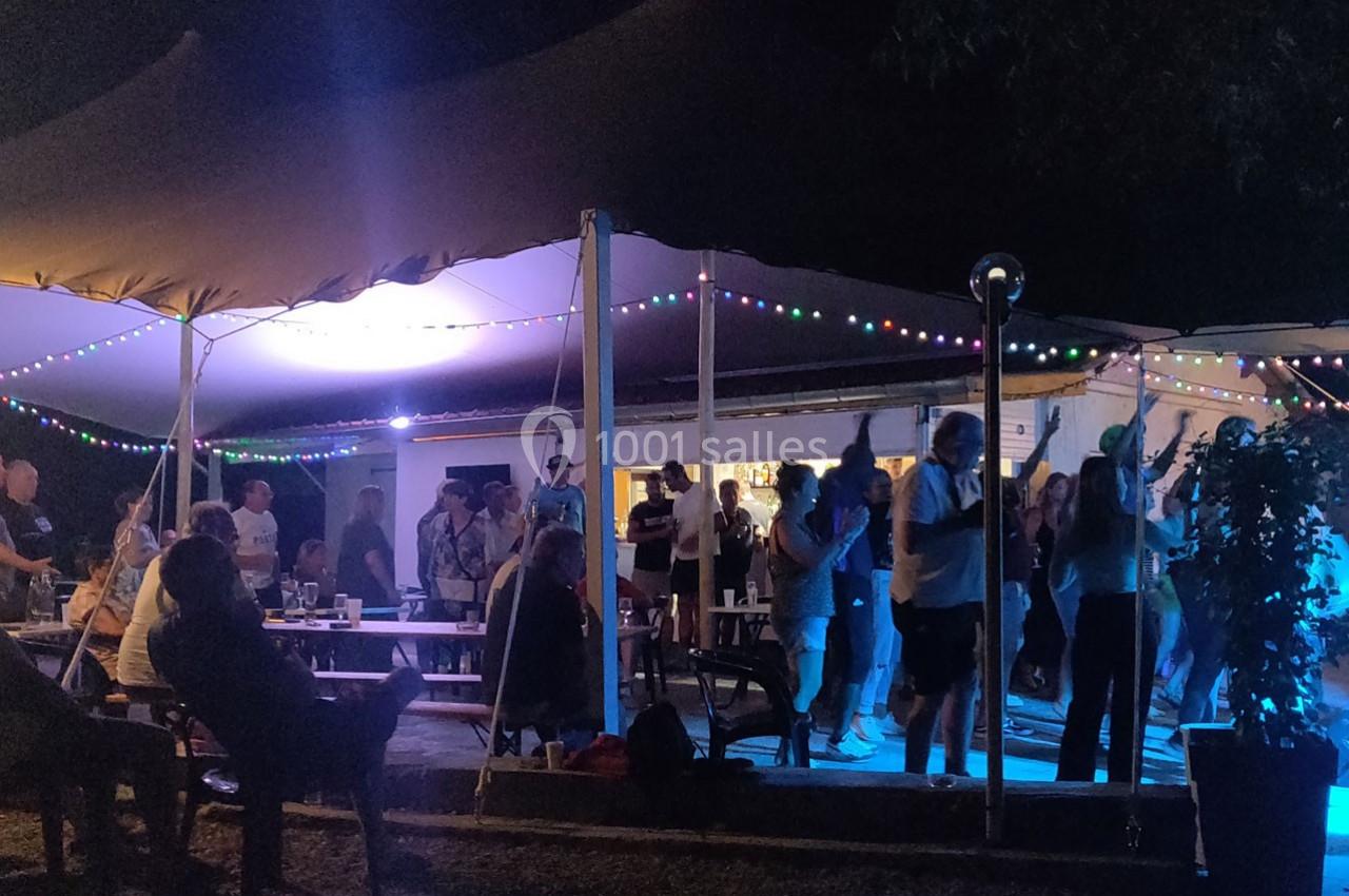 Groupe de personnes dansant et discutant sous une tente éclairée par des guirlandes lumineuses lors d'un événement nocturne.