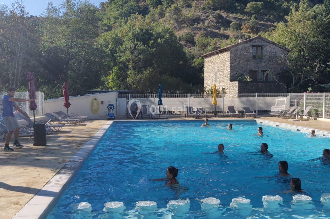 Des personnes nagent et se détendent dans une piscine extérieure entourée de chaises longues et d'arbres.