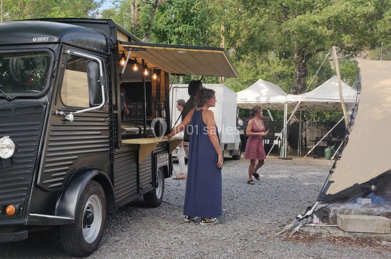 Un food truck noir vintage sert des clients sur un terrain extérieur avec des tentes blanches en arrière-plan.