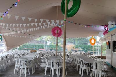 Salle de réception en extérieur décorée pour un événement, avec tables dressées, fleurs et voilages suspendus.