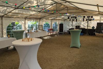 Salle de réception en extérieur décorée pour un événement, avec tables dressées, fleurs et voilages suspendus.