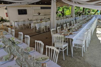 Salle de réception en extérieur décorée pour un événement, avec tables dressées, fleurs et voilages suspendus.