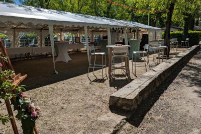 Salle de réception en extérieur décorée pour un événement, avec tables dressées, fleurs et voilages suspendus.