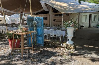 Salle de réception en extérieur décorée pour un événement, avec tables dressées, fleurs et voilages suspendus.