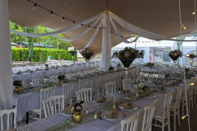 Salle de réception en extérieur décorée pour un événement, avec tables dressées, fleurs et voilages suspendus.