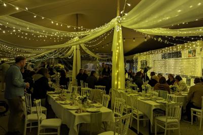 Salle de réception en extérieur décorée pour un événement, avec tables dressées, fleurs et voilages suspendus.