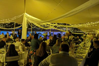 Salle de réception en extérieur décorée pour un événement, avec tables dressées, fleurs et voilages suspendus.