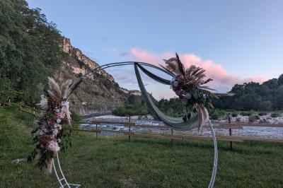 Salle de réception en extérieur décorée pour un événement, avec tables dressées, fleurs et voilages suspendus.