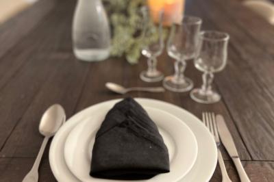 Table dressée avec une assiette blanche, une serviette noire pliée, des couverts, des verres et une carafe d'eau.