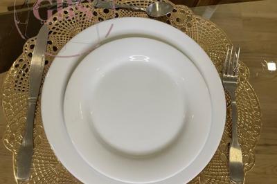 Assiette blanche posée sur un napperon doré, accompagnée de couverts en métal sur une table en verre.