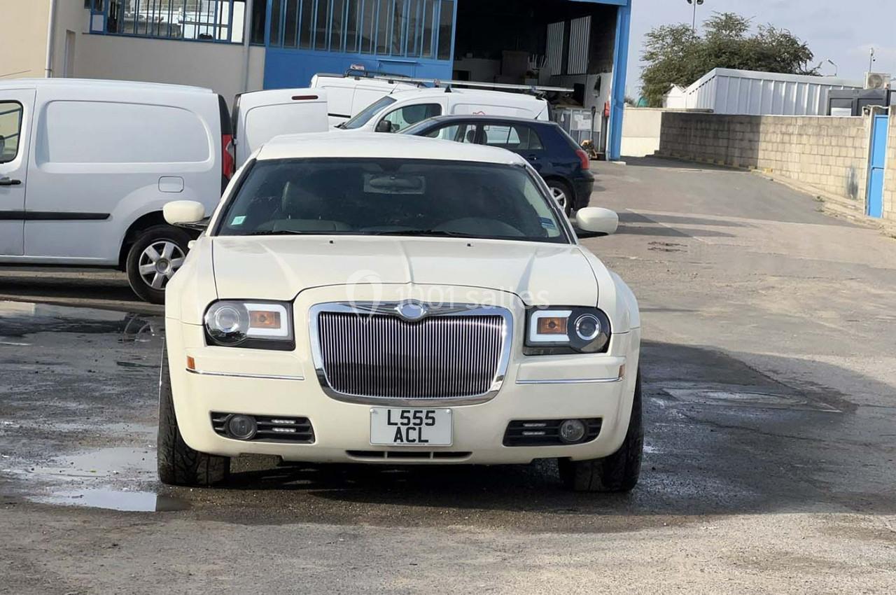 Voiture blanche garée sur un parking extérieur avec des bâtiments industriels en arrière-plan.