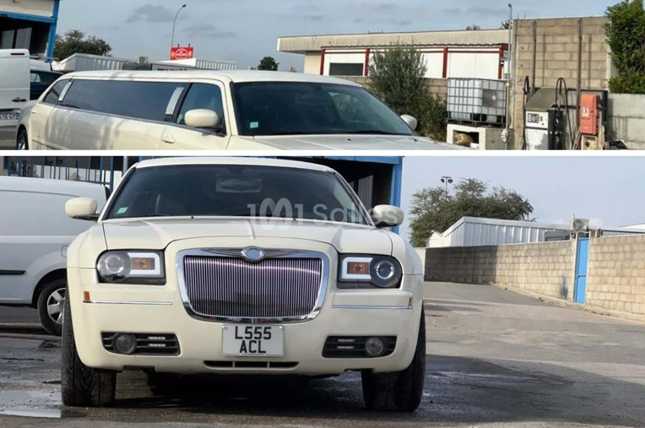 Voiture blanche de luxe, type limousine, stationnée devant un bâtiment industriel avec un parking en arrière-plan.