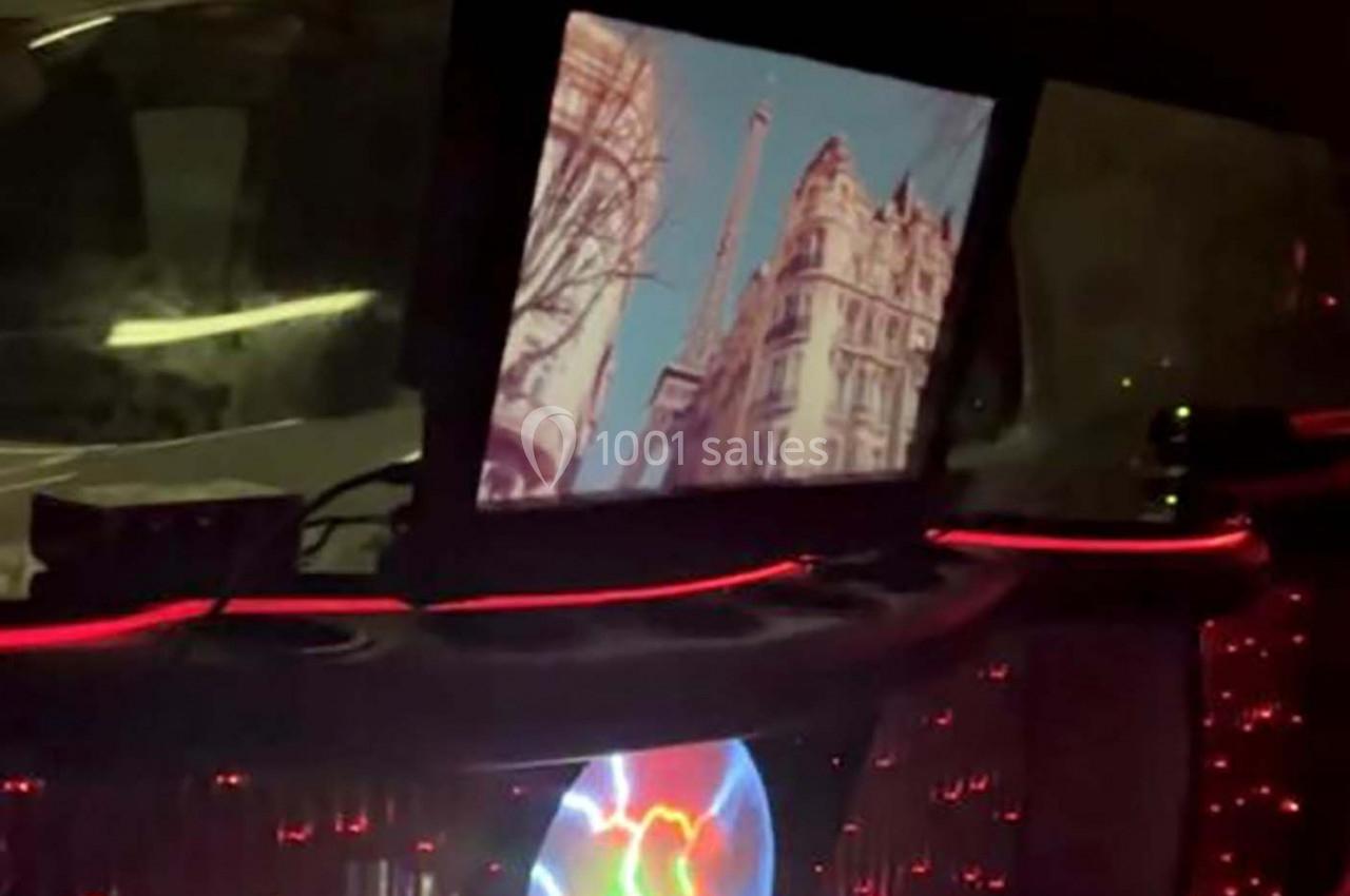 Écran affichant une vue de la Tour Eiffel entourée d'immeubles, dans un intérieur sombre éclairé par des lumières rouges.