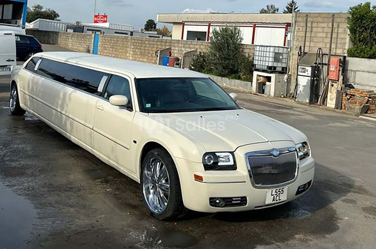 Limousine blanche stationnée sur un sol bétonné dans un environnement industriel.