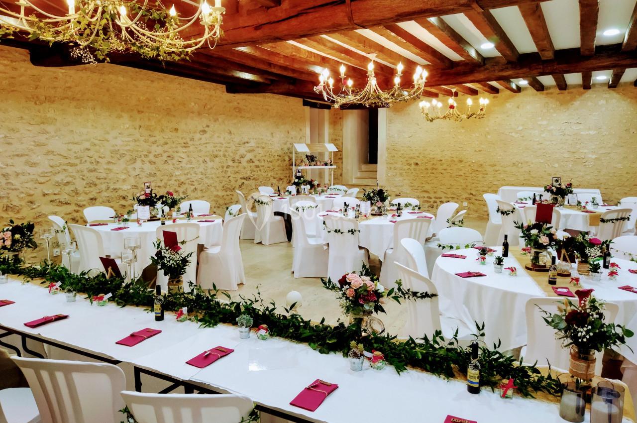 Salle de réception décorée avec des tables rondes, nappes blanches, centres de table fleuris et guirlandes lumineuses.