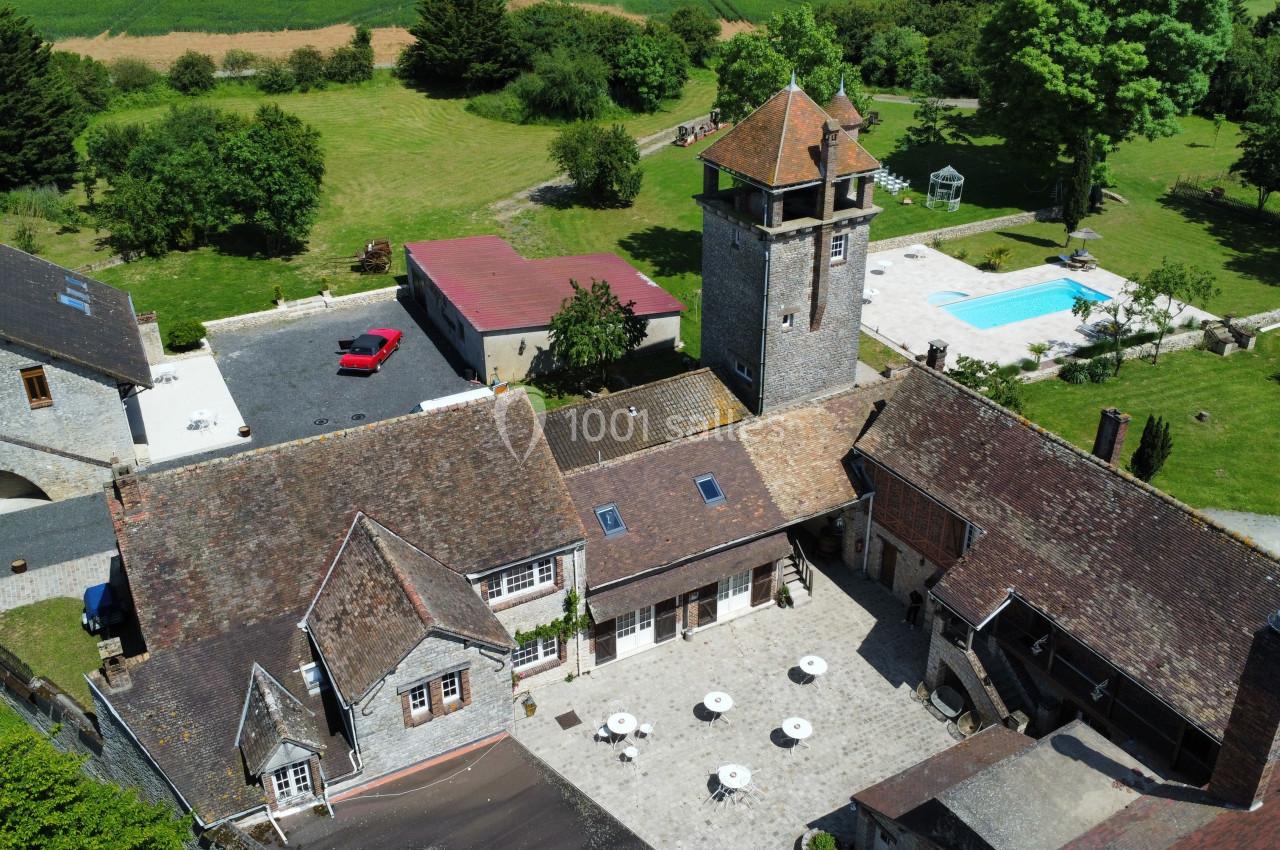 Vue aérienne d'un domaine rural avec bâtiments en pierre, une tour, une piscine et des espaces verts environnants.
