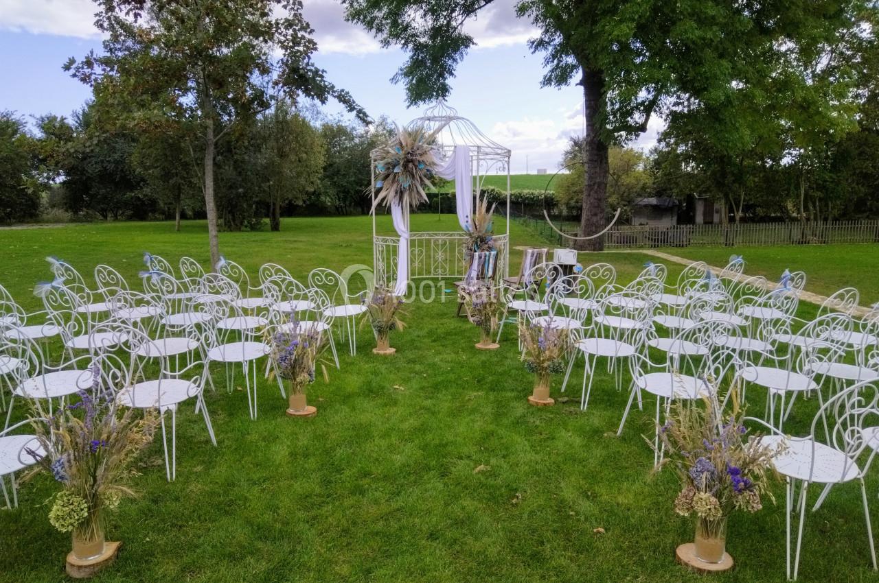 Chaises blanches disposées en allée sur une pelouse, menant à une arche décorée pour une cérémonie en plein air.