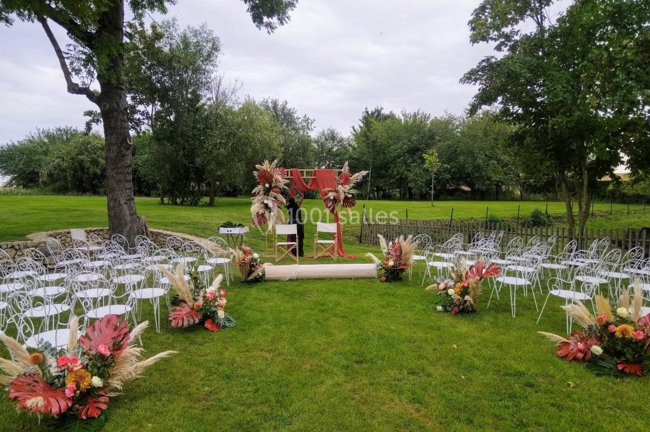 Cérémonie en plein air avec arche décorée de fleurs séchées, entourée de chaises blanches sur une pelouse verte.