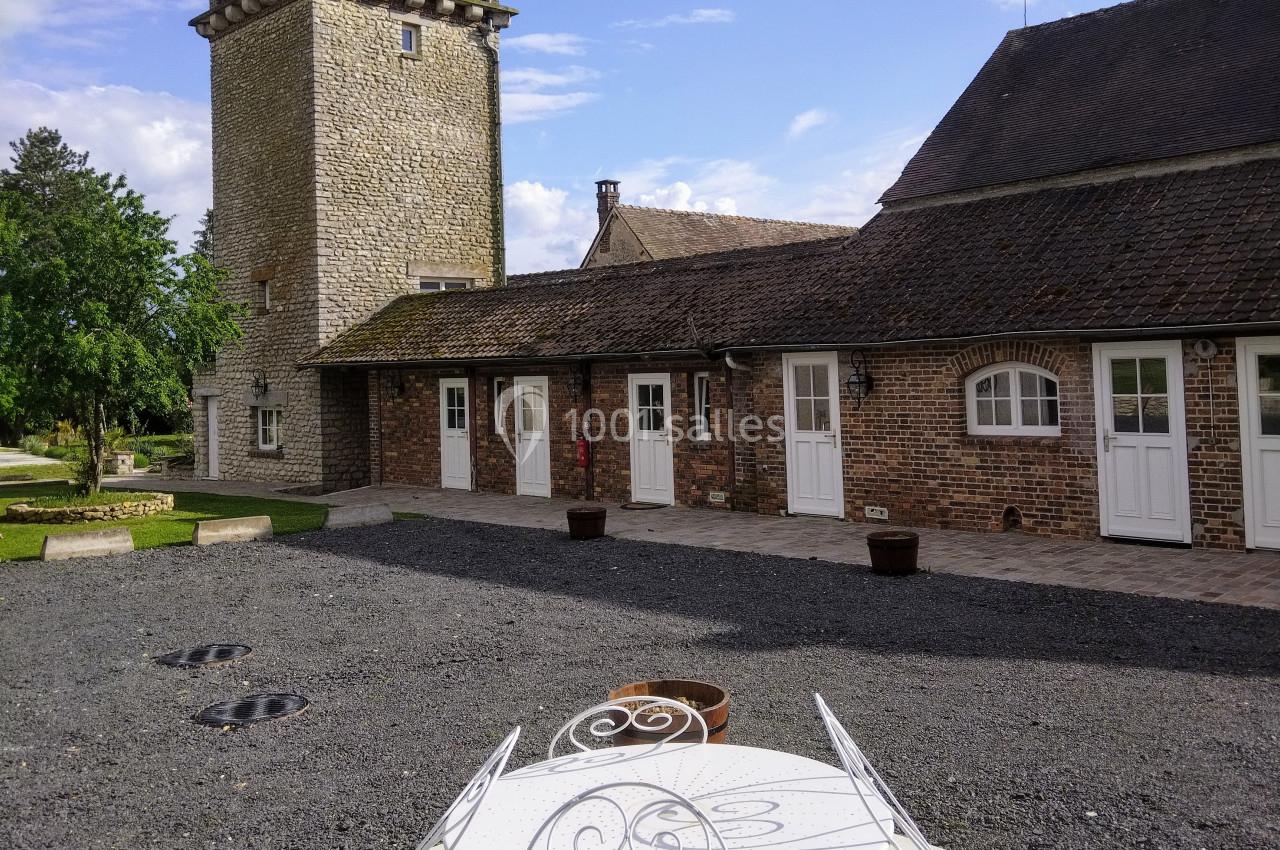 Cour pavée avec une table blanche en fer forgé au premier plan, une tour en pierre et des bâtiments en briques en arrière…