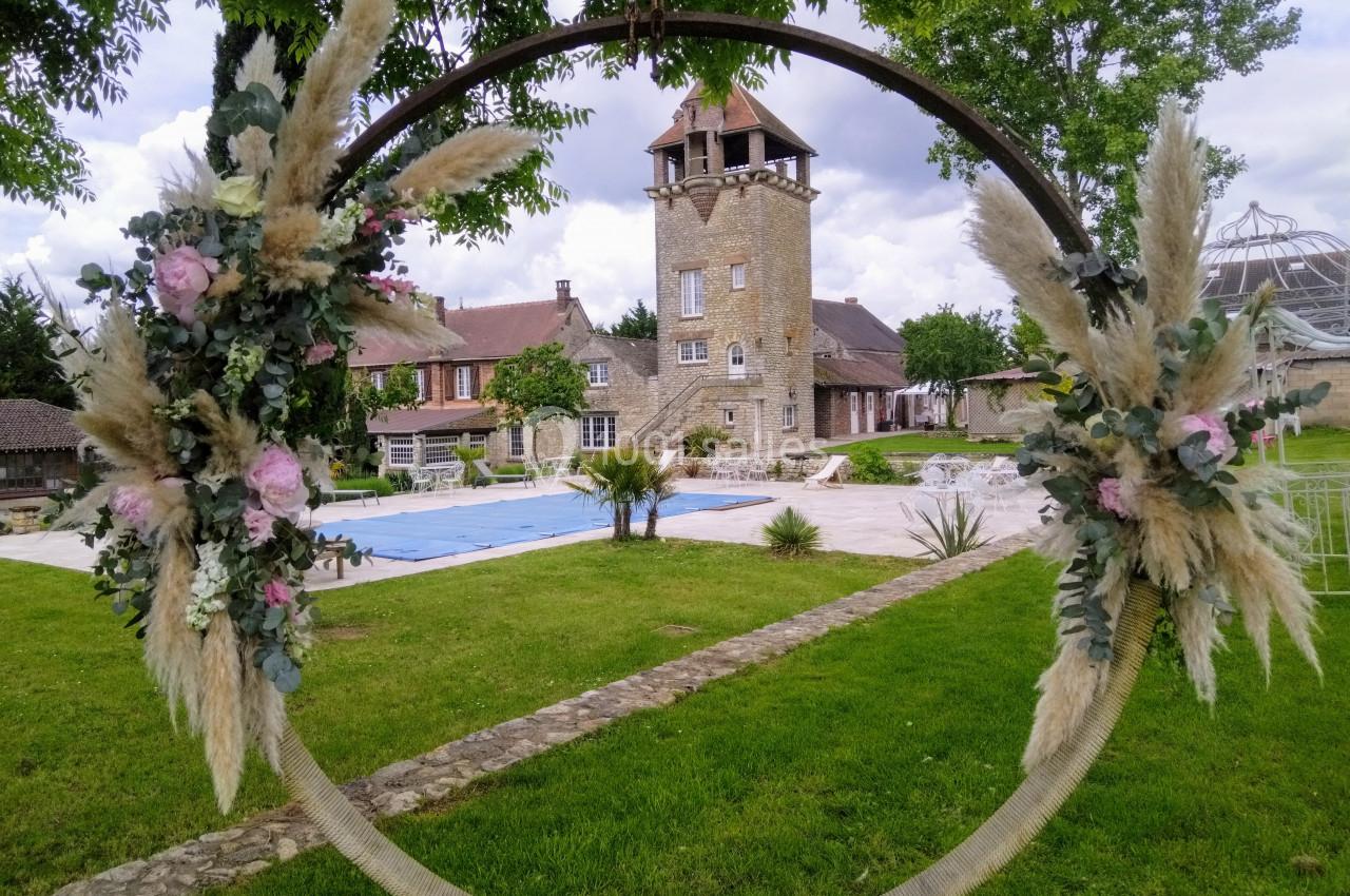 Cercle décoratif fleuri encadrant une vue sur un jardin verdoyant, une piscine et une bâtisse en pierre avec une tour.