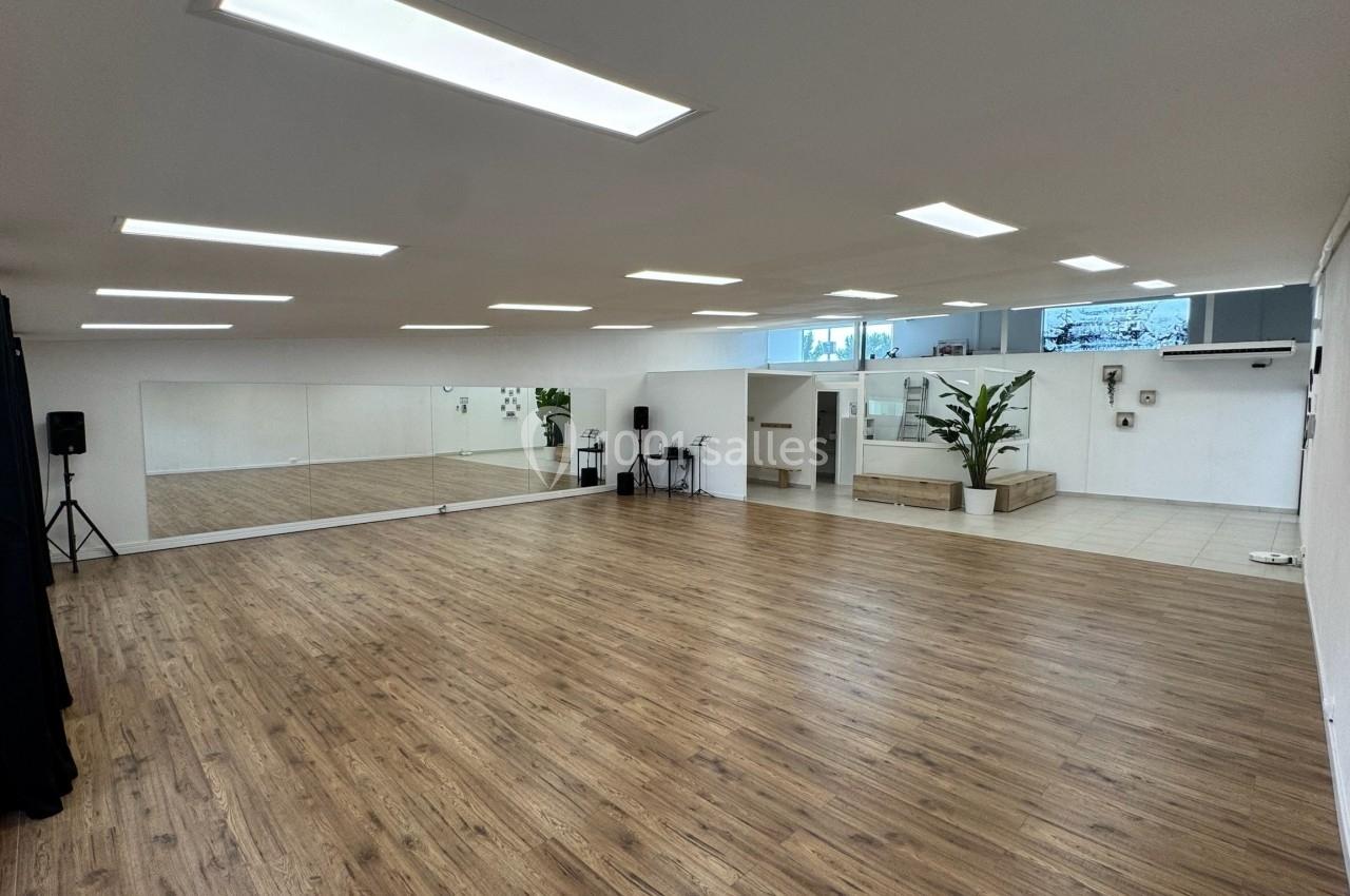 Salle lumineuse avec parquet, grands miroirs muraux, plantes et éclairage au plafond.
