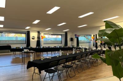 Salle lumineuse avec parquet, murs blancs, plantes décoratives et grandes fenêtres laissant entrer la lumière naturelle.