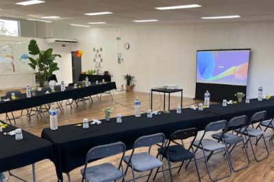 Salle lumineuse avec parquet, murs blancs, plantes décoratives et grandes fenêtres laissant entrer la lumière naturelle.