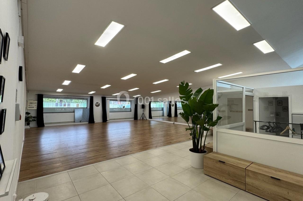 Salle lumineuse avec parquet, murs blancs, plantes décoratives et grandes fenêtres laissant entrer la lumière naturelle.