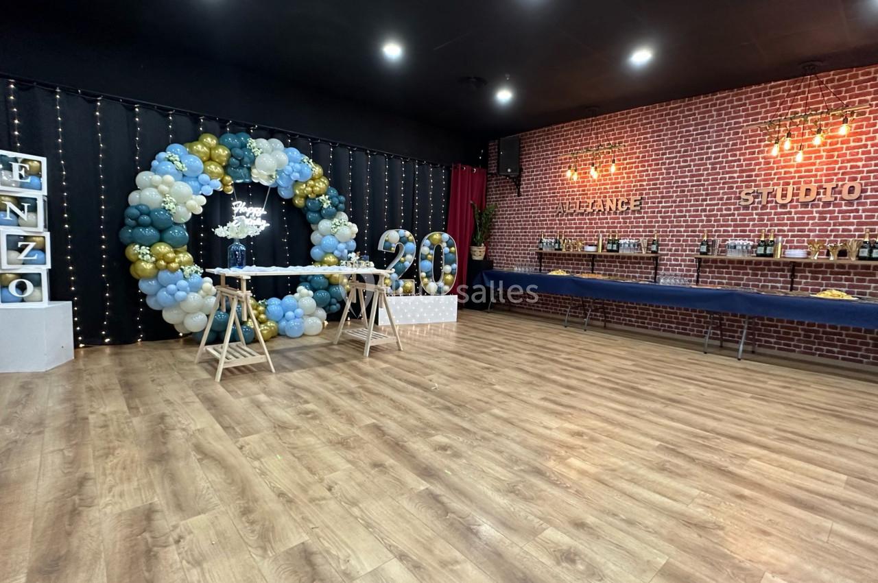 Salle décorée pour une fête avec arche de ballons, table, chiffres ’20’ lumineux et murs en briques.