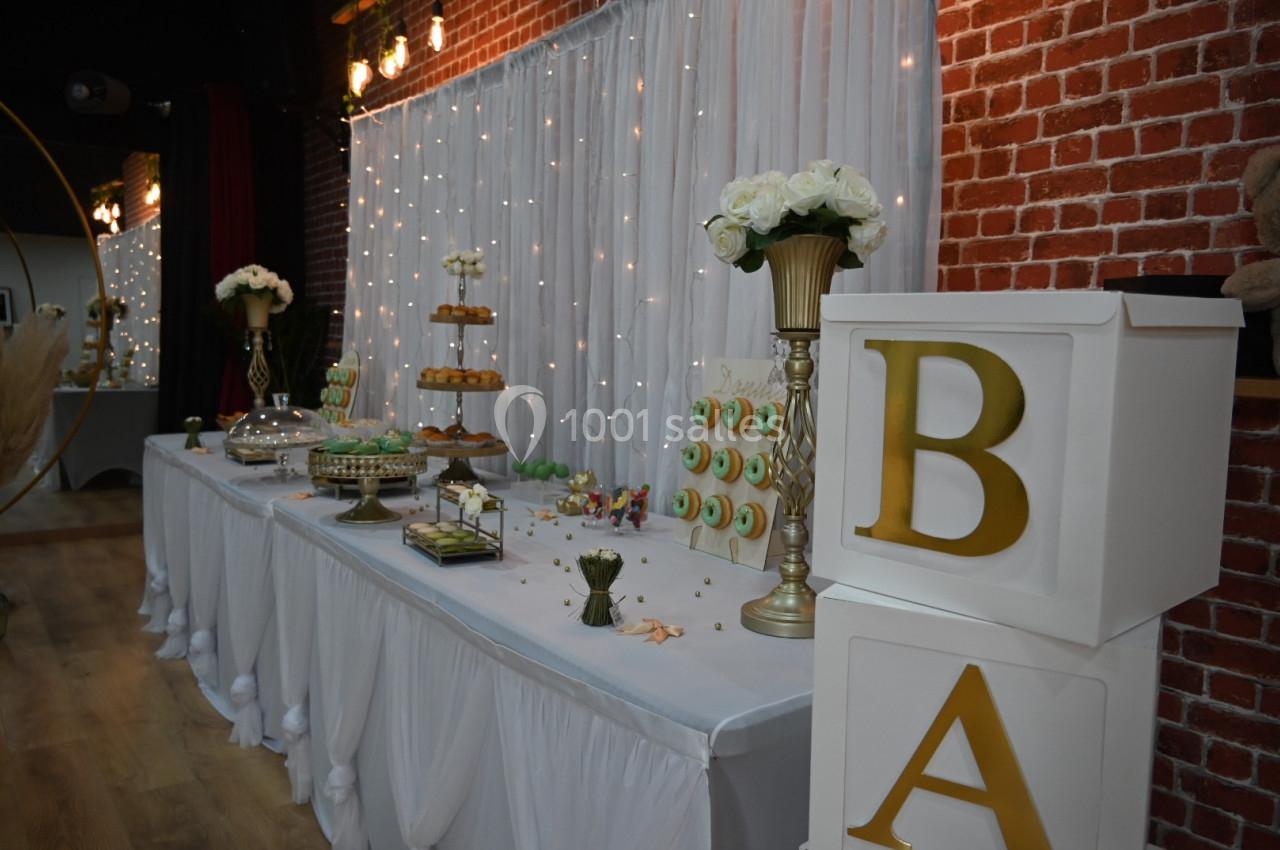 Table décorée pour une réception, avec pâtisseries, fleurs et boîtes blanches ornées de lettres dorées.