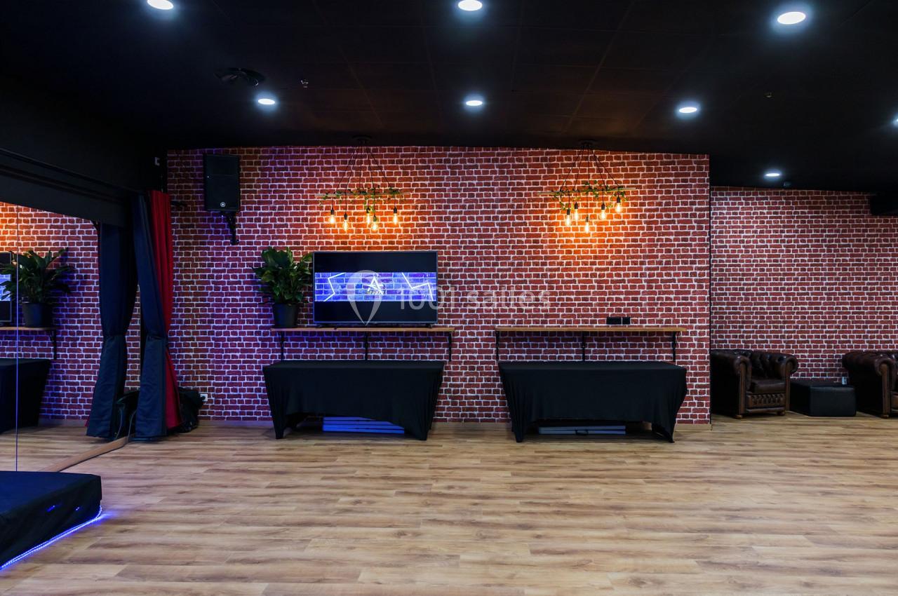Salle avec mur en briques rouges, sol en bois, tables recouvertes de nappes noires et fauteuils en cuir marron.