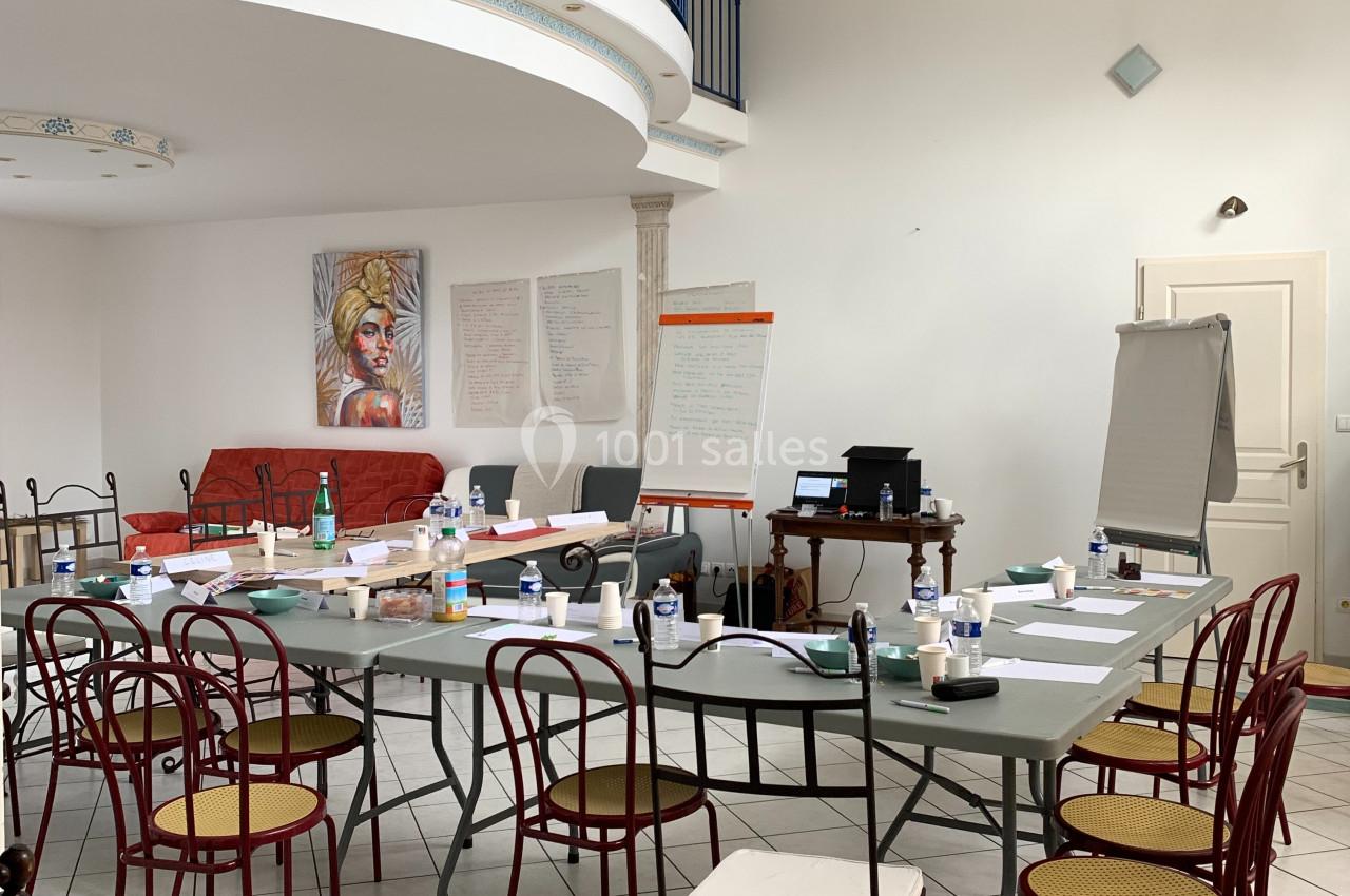 Salle lumineuse aménagée pour une réunion, avec une grande table entourée de chaises et des supports de présentation.