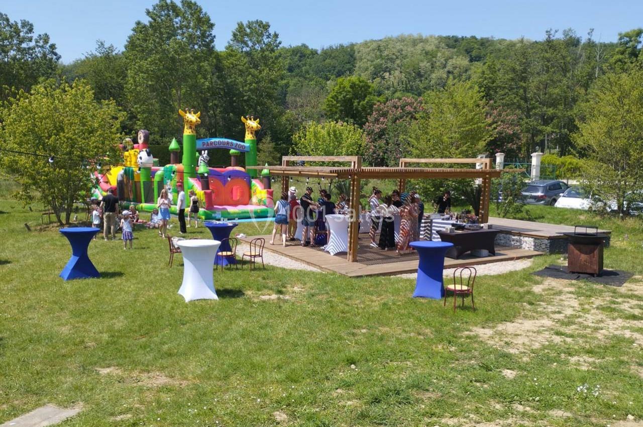 Personnes rassemblées autour de tables en extérieur près d'un château gonflable dans un cadre verdoyant.