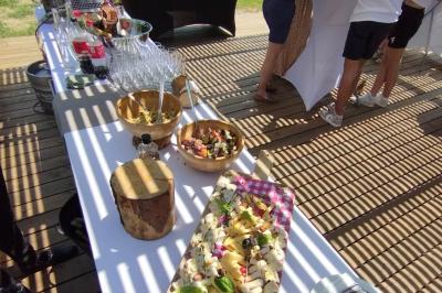 Espace extérieur couvert par une tente beige, avec des tables et des personnes assises dans un cadre verdoyant.