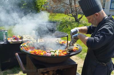 Espace extérieur couvert par une tente beige, avec des tables et des personnes assises dans un cadre verdoyant.
