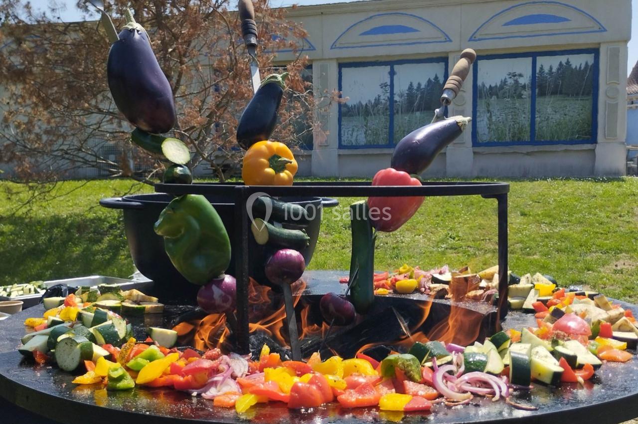 Légumes variés cuits sur un brasero en plein air, avec un bâtiment peint en arrière-plan.